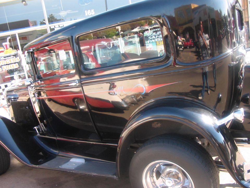 Black sedan with red pinstriping on the side. Chrome wheels and trim. Reflection shows a building with a sign that says '165'