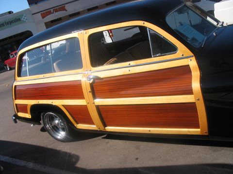 1986 Ford Bronco - A classic woodie station wagon with a black roof and extensive wood paneling is seen from the side.