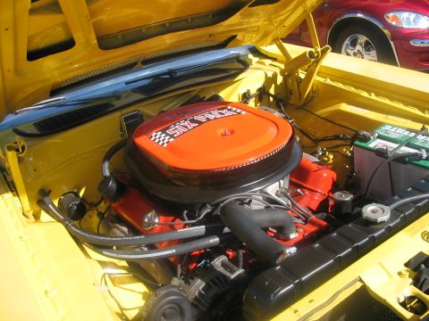 1986 Ford Bronco - Engine bay of a yellow car, a V8 engine and an orange "SIX PACK" air cleaner. Another vehicle is partially visible.