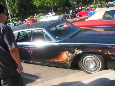1986 Ford Bronco - A man stands next to a heavily customized classic car a skull and flame graphic on its side.