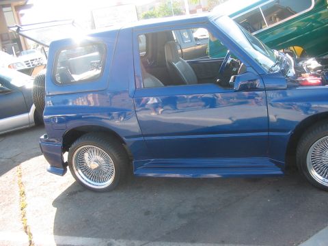 1986 Ford Bronco - A blue SUV with custom wire wheels is parked outdoors.