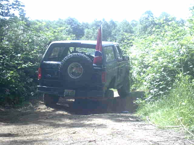 Rear of lifted Ford Bronco with tailgate-mounted spare flexing on wooded trail