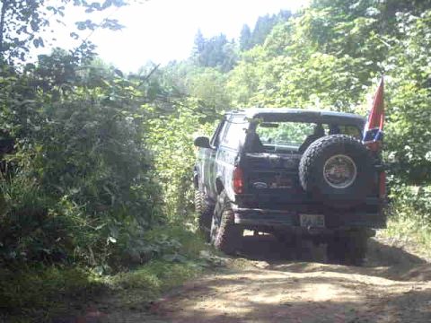 1995 Ford Bronco - This 1995 Ford Bronco is seen from the rear, parked on a dirt road with trees in the background.
