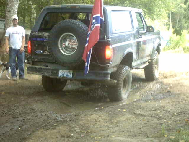 Rear of lifted black Ford Bronco on mud with spare tire and Confederate flag on a pole