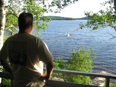 1986 Ford Bronco - A man stands on a porch, gazing out at a tranquil lake surrounded by lush greenery.