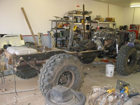 1981 Ford Bronco - 1981 Ford Bronco chassis undergoing modification in a garage setting, showing the frame, engine, and suspension components.