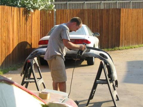 1994 Buick Park Avenue - A man works on a car bumper, with a white sedan visible in the background.