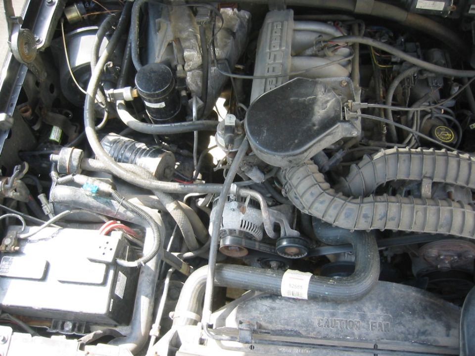 Engine bay with 5.8 EFI intake, alternator, serpentine belt, battery, and fan shroud marked CAUTION FAN