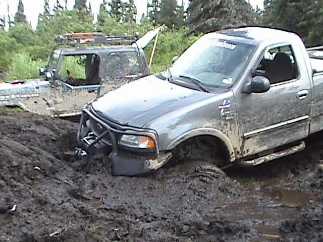 Ford F-150 and Jeep Wrangler stuck in deep mud, trees in background