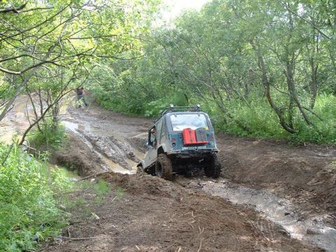 2000 Jeep Wrangler - A Jeep Wrangler TJ tackles a challenging muddy off-road course surrounded by dense foliage.