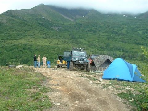 2000 Jeep Wrangler - A 2000 Jeep TJ is parked at a campsite with tents set up, overlooking a vast mountainous landscape.