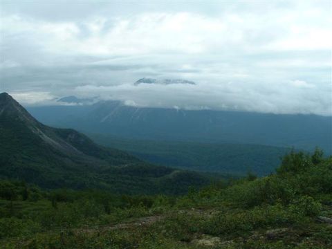 2000 Jeep Wrangler - A vast mountain landscape under a cloudy sky, with trees in the foreground and a website logo at the bottom.