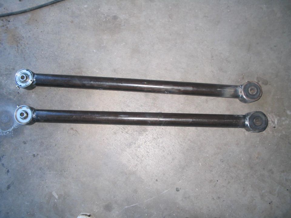 Pair of tubular steel control arms with rubber bushings lying on a concrete garage floor