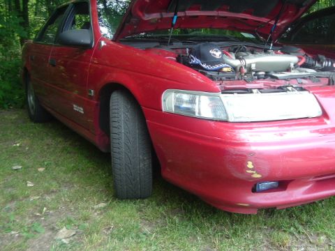 1993 Ford Taurus - A red 1993 Ford Taurus sedan is shown from the front quarter angle with its hood open, parked on a grassy area.