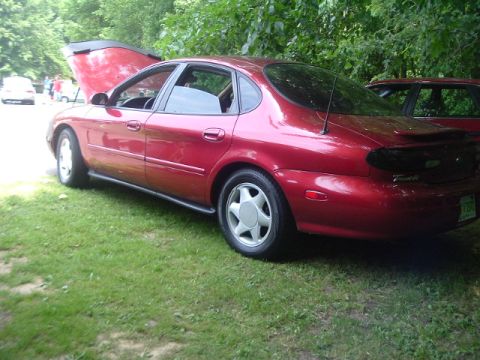 1993 Ford Taurus - Red sedan with hood open, parked on grass with another vehicle nearby.