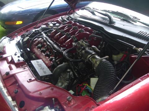 1993 Ford Taurus - Close-up of a V6 engine in a red car's engine bay, with another vehicle in the background.