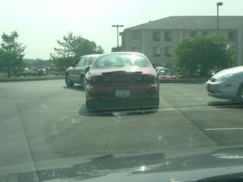 1993 Ford Taurus - Rear view of a red sedan with a spoiler, parked in a lot next to other vehicles.