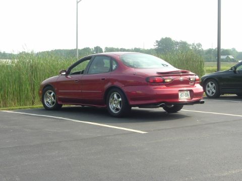 1993 Ford Taurus - This red sedan, likely a 1996 Ford Taurus, is parked in a lot next to another vehicle. The license plate reads 657-DON.