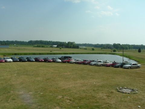 1993 Ford Taurus - A gathering of vehicles parked in a field beside a body of water on a clear day.