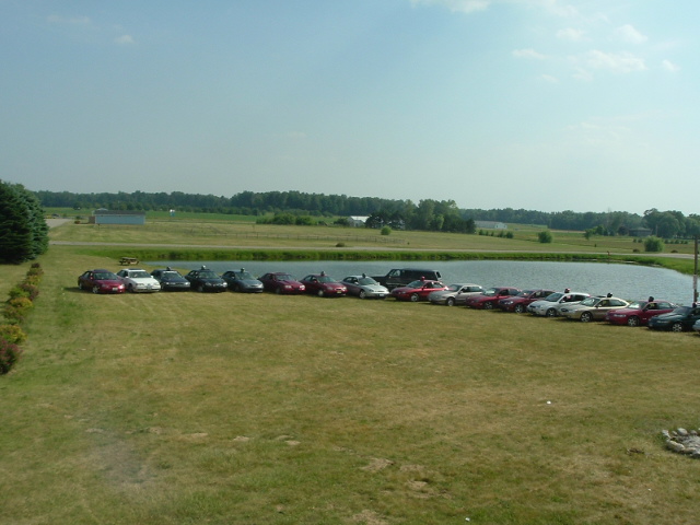 many cars parked in a row on grass next to a lake