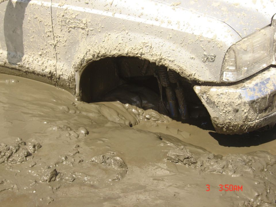 Light SUV stuck deep in brown mud, front fender and headlight visible above the muck