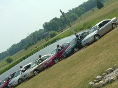 1993 Ford Taurus - Multiple sedans are parked in a row on a grassy incline beside a body of water under a bright sky.