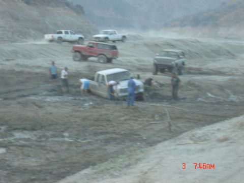 1977 Toyota Land Cruiser - Multiple trucks are stuck in a muddy area, with several people gathered around trying to help.