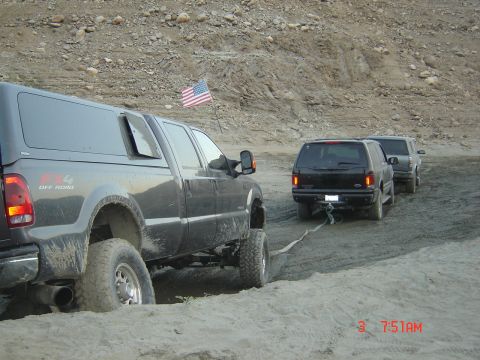 1977 Toyota Land Cruiser - A pickup truck tows two SUVs through a sandy terrain, with an American flag flying nearby.