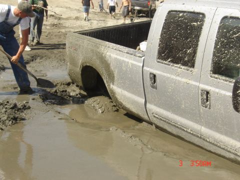 1977 Toyota Land Cruiser - A silver pickup truck is stuck in deep mud, with a person attempting to dig it out.