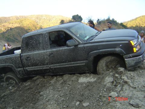 1977 Toyota Land Cruiser - A black pickup truck is stuck in thick mud, with people observing the scene.