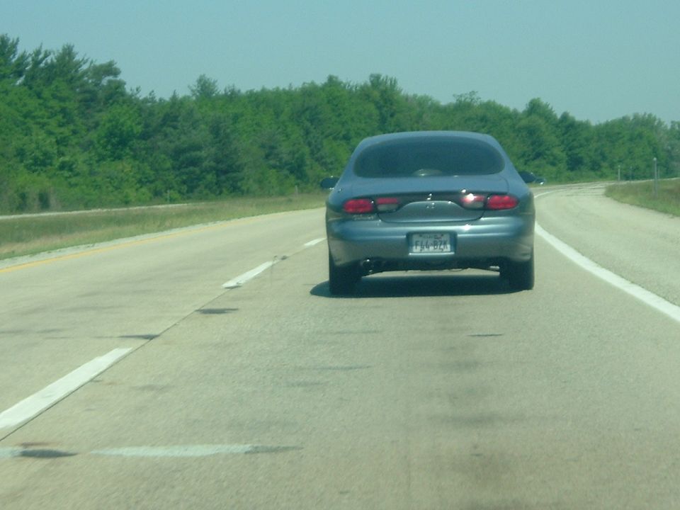 1993 Ford Taurus driving on a highway, rear view. License plate is visible