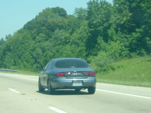 1993 Ford Taurus - The rear view of a blue sedan with a license plate F54-BZA driving on a highway.