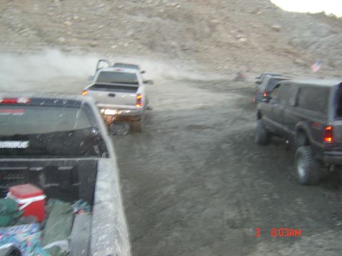 1977 Toyota Land Cruiser - Several trucks and SUVs navigate a dusty off-road trail, with one vehicle in the foreground showing its bed contents.