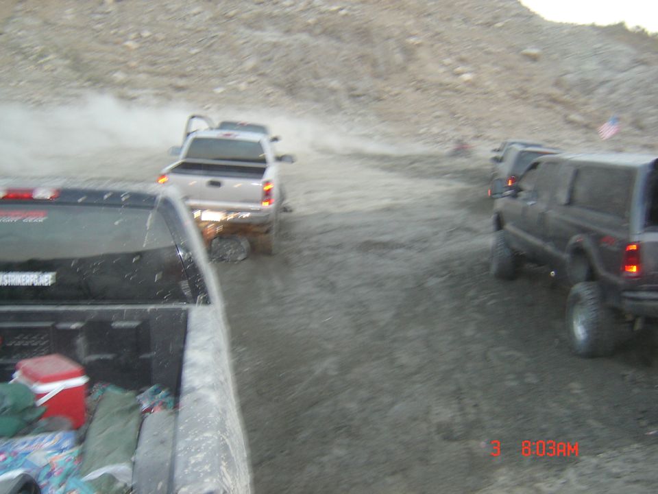 View over pickup bed of white truck and lifted Jeep Cherokee on dusty off-road trail