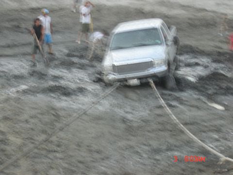 1977 Toyota Land Cruiser - A truck is stuck in thick mud, with several people attempting to free it using ropes.