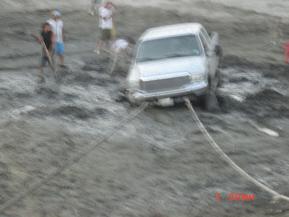 White full-size Ford SUV buried in gray mud with two recovery straps attached to the front