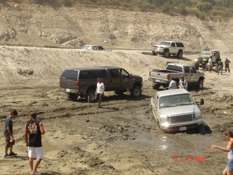 1977 Toyota Land Cruiser - Multiple trucks are stuck in a muddy area, with some vehicles partially submerged in the mire.