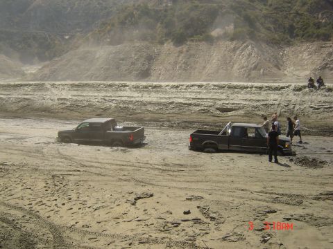 1977 Toyota Land Cruiser - Two pickup trucks are stuck in a muddy area, with several people attempting to free one of them.