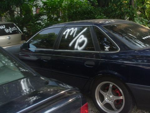 1993 Ford Taurus - A dark blue sedan is parked outdoors, with white spray paint on its rear window.