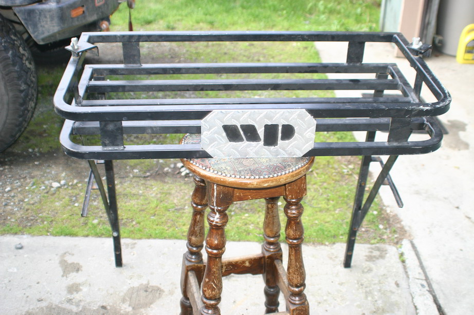 Black metal roof rack with diamond plate WP logo, resting on a wooden stool