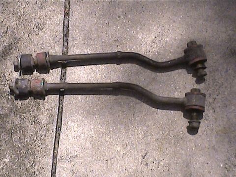 1978 Ford Bronco - A pair of automotive suspension control arms are displayed on a concrete background.