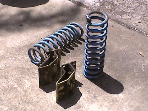 1978 Ford Bronco - Two blue coil springs and associated metal brackets are displayed on a concrete surface.