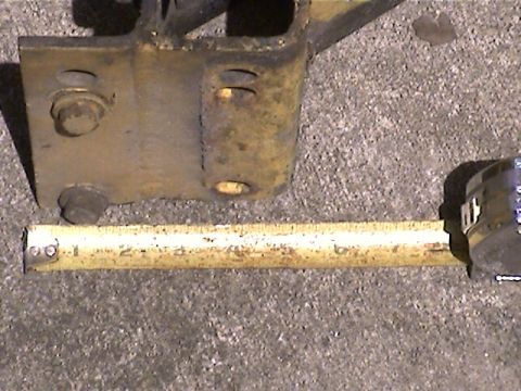 1978 Ford Bronco - A metal bracket is measured against a concrete background.