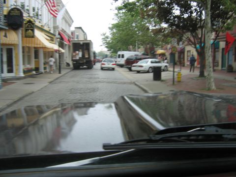 1976 GMC C/K Pickup - View from inside a vehicle shows a reflection of a street lined with shops and other cars.