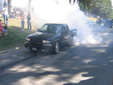 1976 GMC C/K Pickup - A black pickup truck performs a burnout, creating a large cloud of smoke.