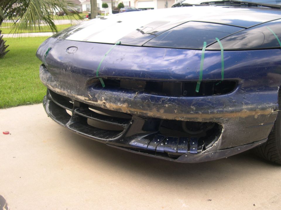 Front bumper of a blue car, looks like it needs repair. Green tape is holding parts of it together