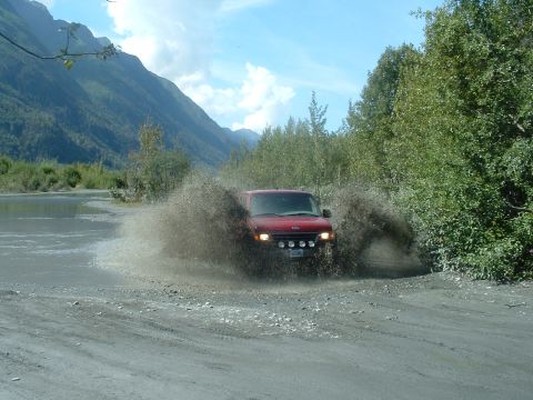 1994 Ford E350 - A red van navigates a muddy off-road path, sending water and dirt flying.