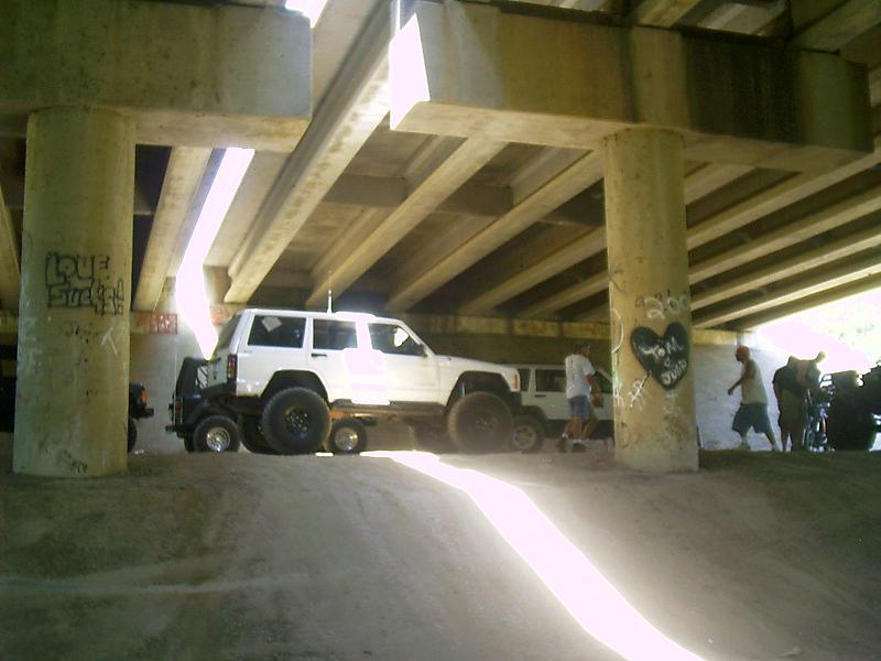 White Jeep Cherokee parked under a bridge, with another vehicle behind it