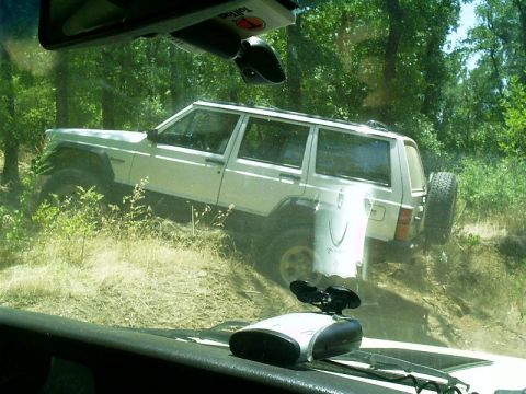 1986 Ford Bronco - White Jeep Cherokee navigating an off-road trail with a spare tire on the back.