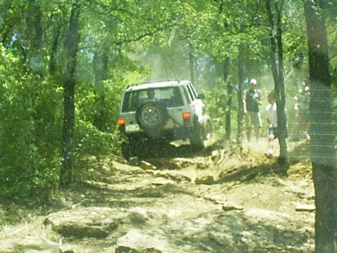 1986 Ford Bronco - An off-road vehicle navigates a challenging, rocky path through a dense forest.